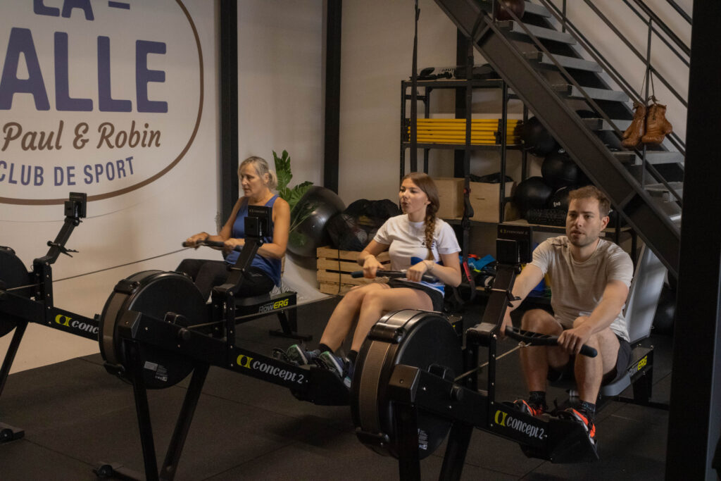 3 pratiquants qui font du rameur à la salle