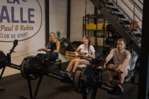 3 pratiquants qui font du rameur à la salle